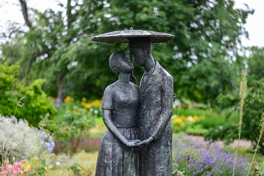 Skulptur eines Paares im Regen unter einem Regenschirm im Garten stehend.